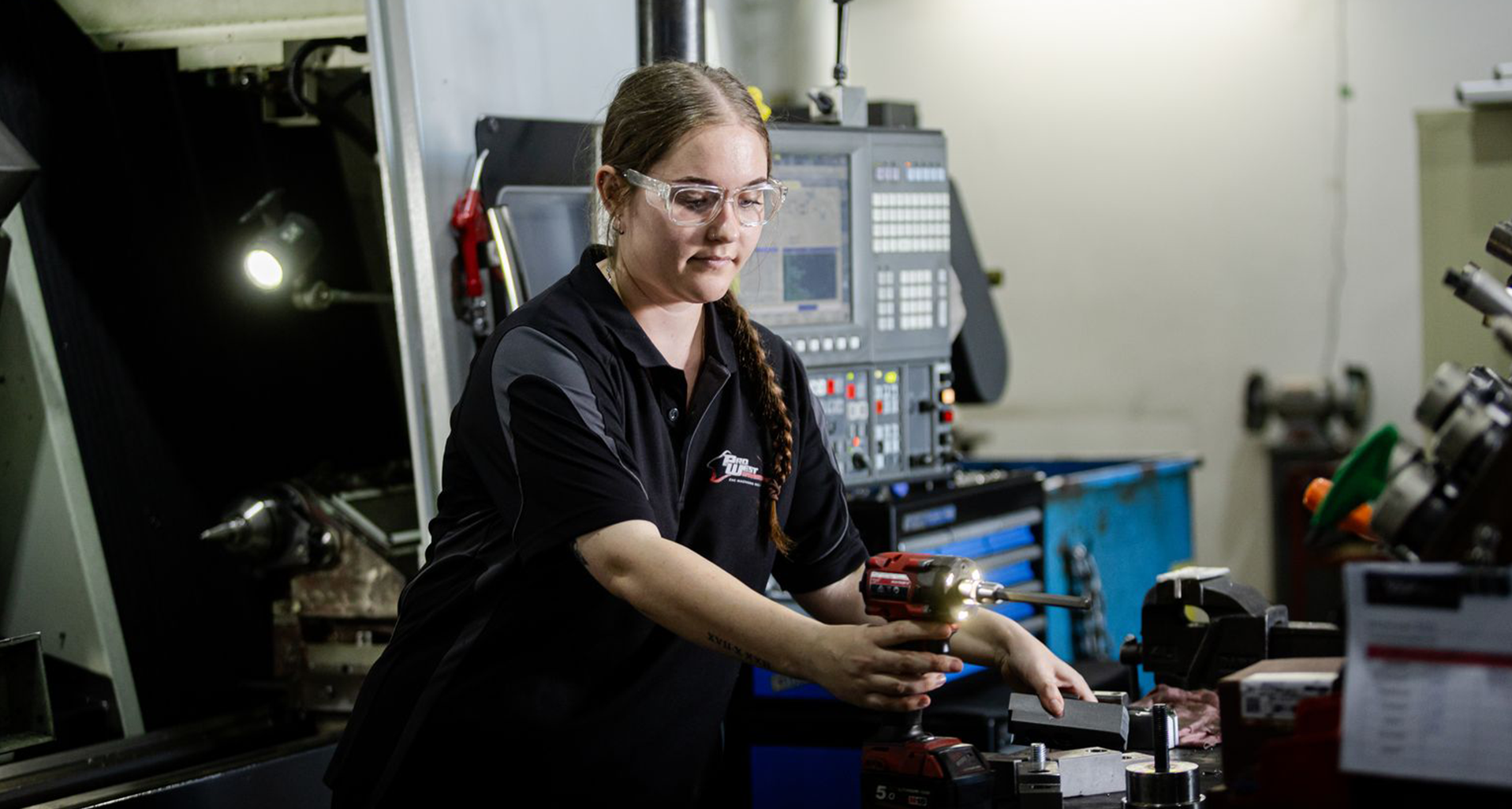 Person using a power drill while working with metal parts in a machining workshop.