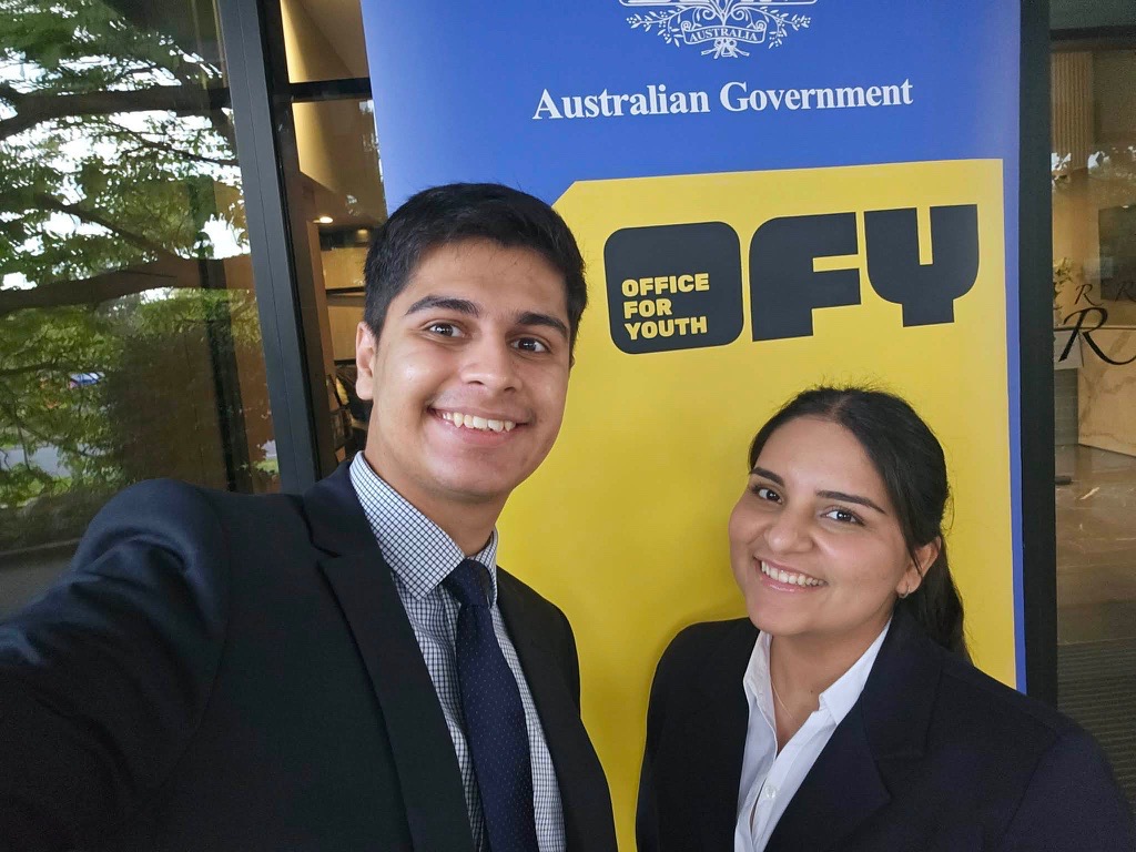 Two members of the Ministerial Youth Advisory Council taking a selfie in front of the Office for Youth pull-up banner.