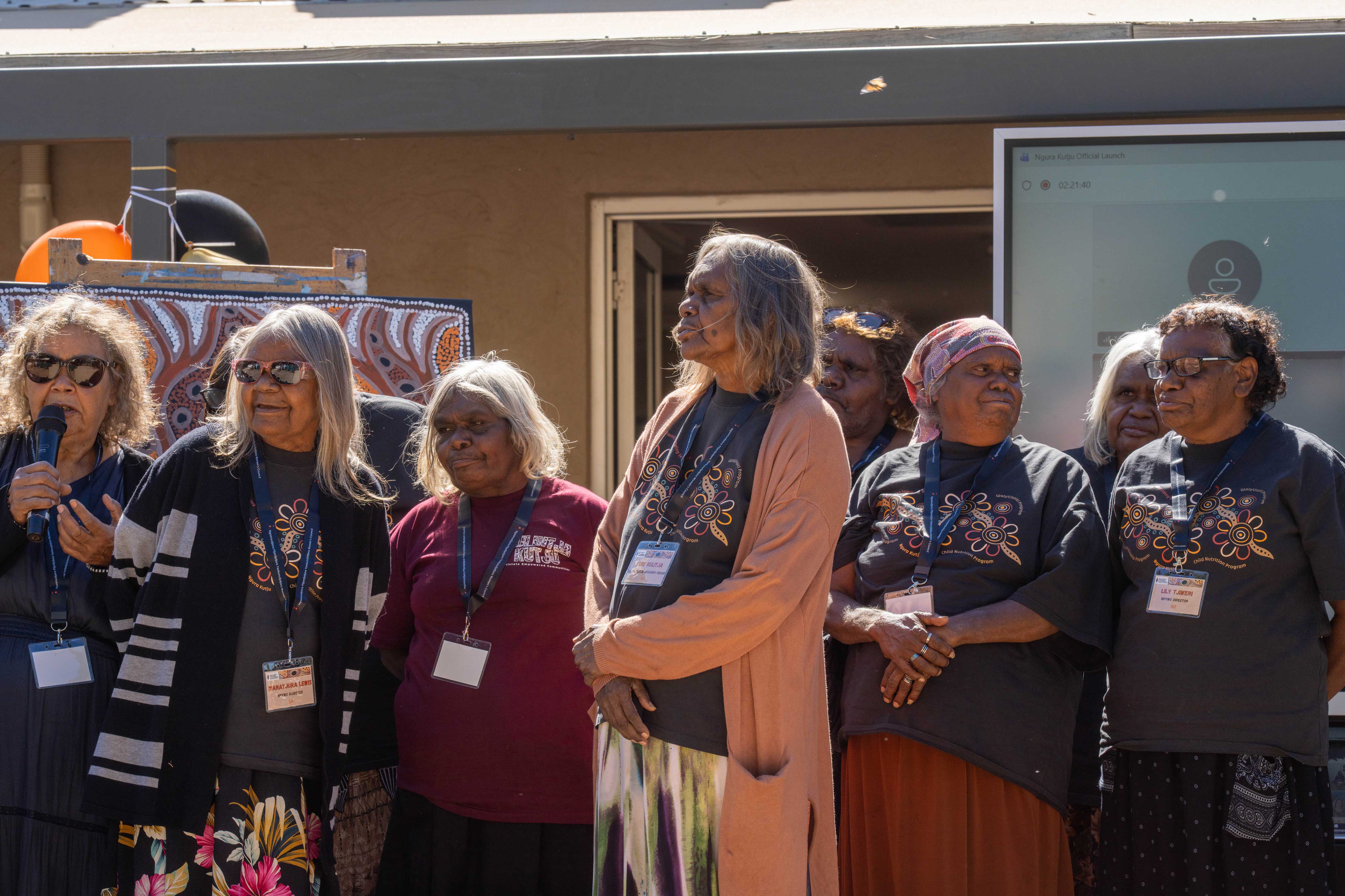 a group of Aboriginal women in an outdoor setting, watching an opening event