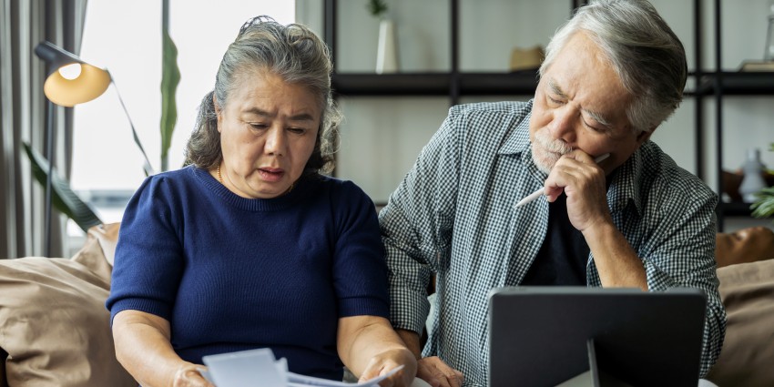 An older couple are sitting on a couch together, completing filing and paperwork.
