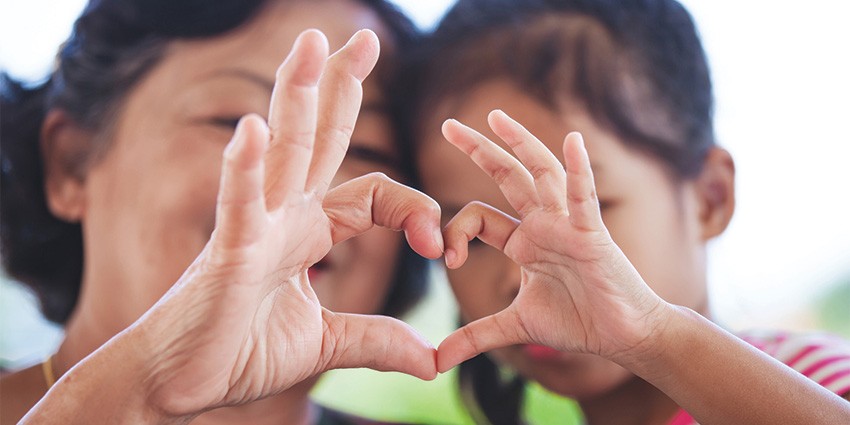 A woman and a child with their hands forming a love heart shape