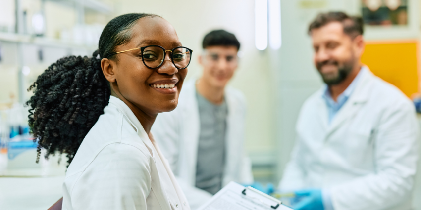 Woman in a laboratory holding a clipboard. Behind her are two other scientists.