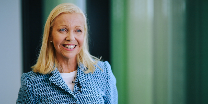 A portrait of Donna Cross wearing a blue patterned blazer. Behind her is a soft green coloured background.