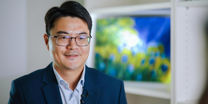 Portrait of Professor Hongqi Sun in a suit. In the background is a blurred blue, yellow and green painting.