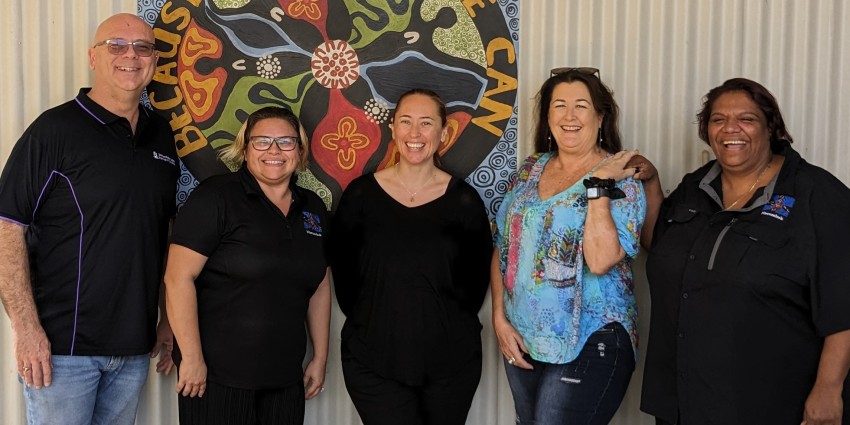Five people standing in front of a wall and a bright painting.