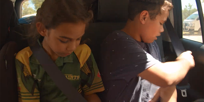 two young people sitting in a car, one with a seatbelt already on, the other in the process of securing their seatbelt.