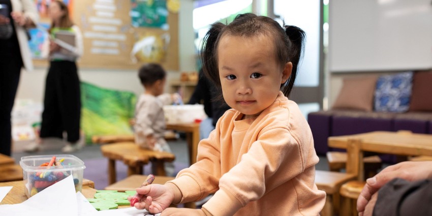 A young child sitting at a table, drawing with coloured crayons.