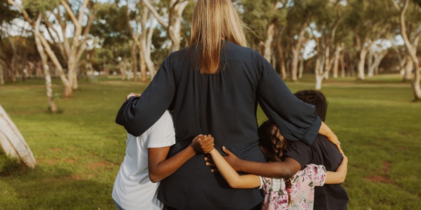 a woman with her arms around three young children on a grass field