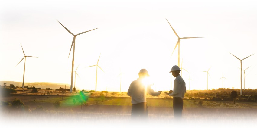 "Sectoral Emission Reduction Strategies - two men in hard hats stand in front of wind turbines. The sun is low on the horizon, a new day is dawning. Could these men, in their clean white collared shirts bring about the change in our energy system in time to hit emission targets? Is that rising sun actually a setting sun? Only time will tell, unless the answer is actually on the clipboard they're looking at.