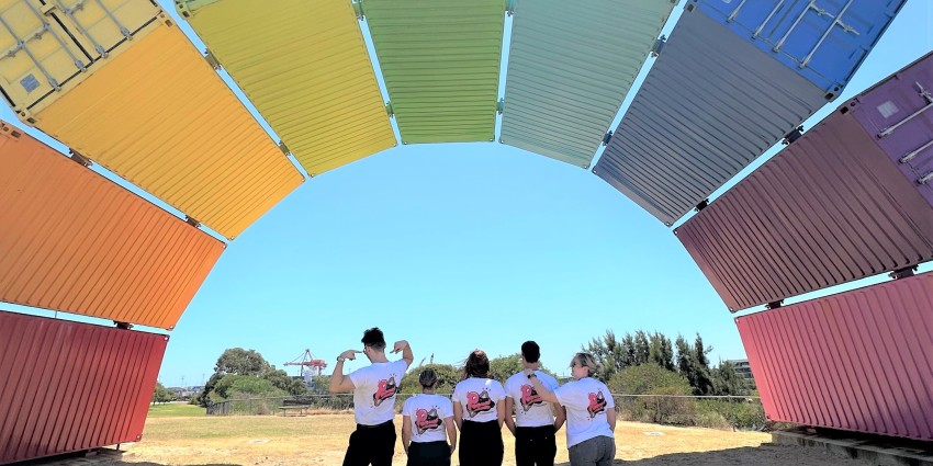 5 people standing under a rainbow made of shipping containers