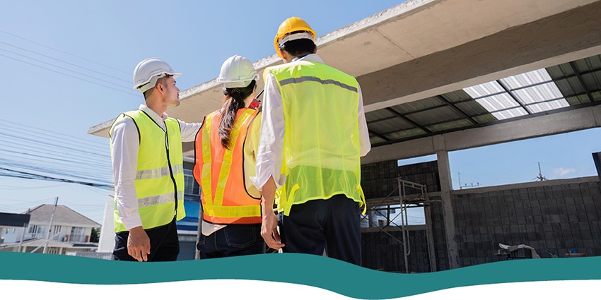 Three people in personal protection equipment (PPE) looking at construction site