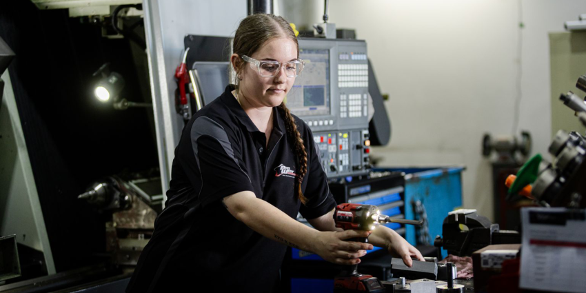 Person using a power drill while working with metal parts in a machining workshop.