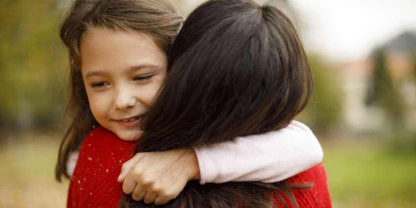 A woman with long hair, holding a young girl in her arms in a warm embrace