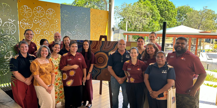 Group of people standing in front of an Aboriginal artwork