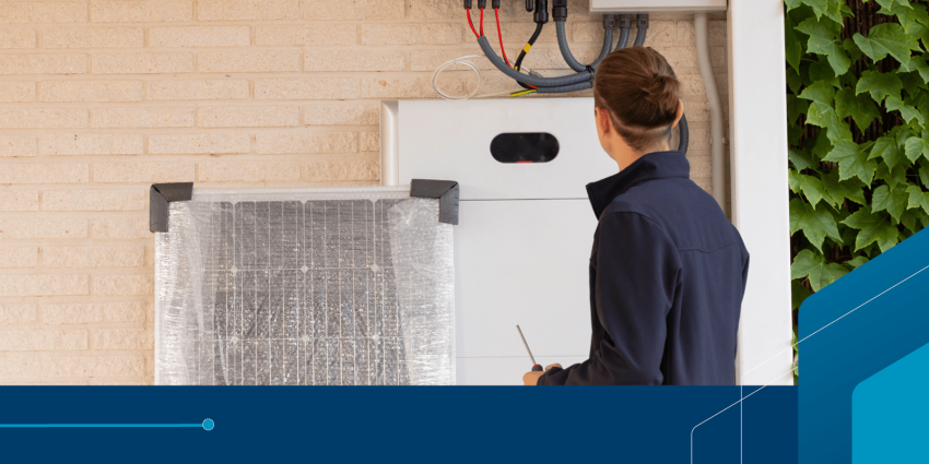 Person in work overalls holding a screwdriver looks at battery installed on the wall of a house
