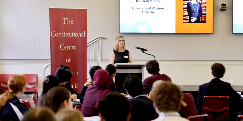 someone is standing at a lectern and speaking to school students in the audience