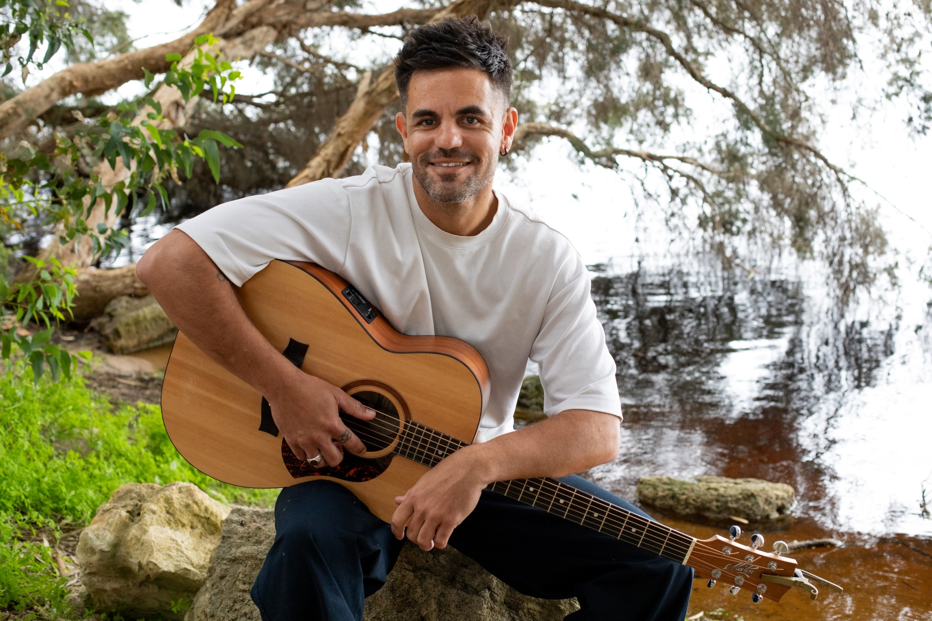 A man in casual clothes in a natural setting holding a guitar